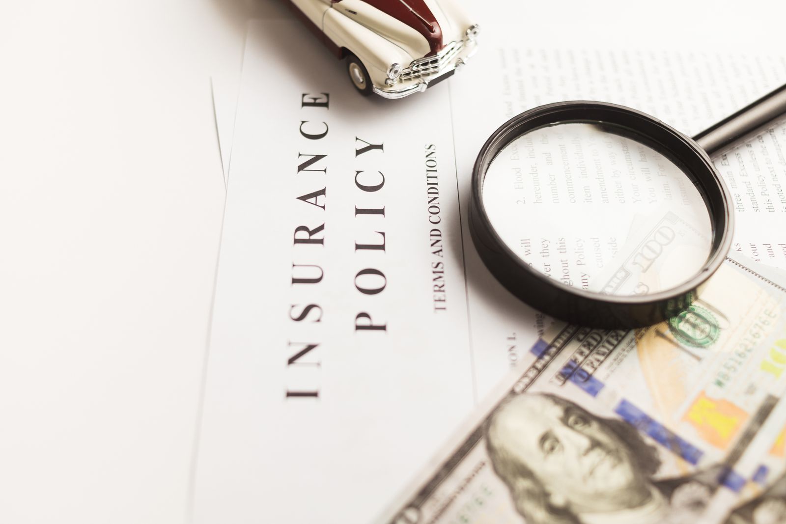 An insurance policy with a magnifying glass, money and a model car