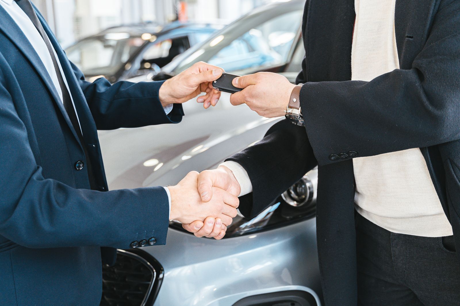 Two people exchanging car keys and shaking hands during a vehicle deal